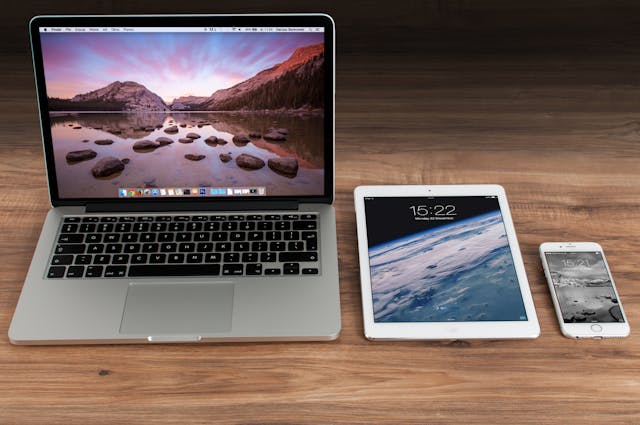 A laptop, a tablet, and a smartphone on a wooden surface.